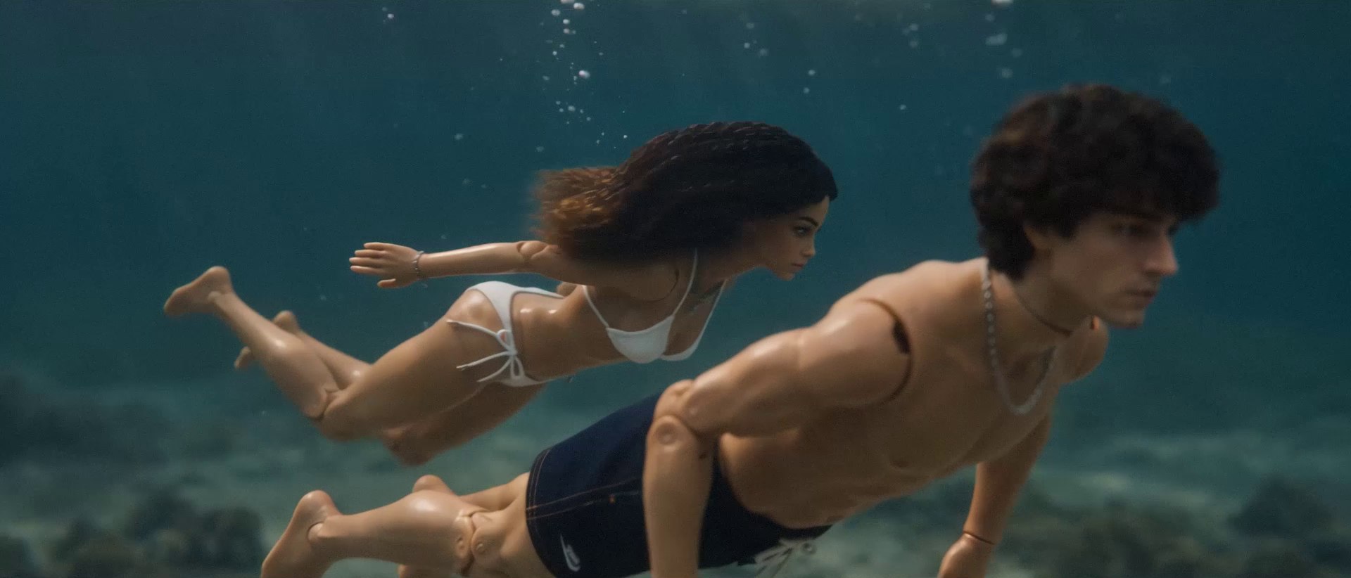 The couple swim underwater side by side through a sunlit reef