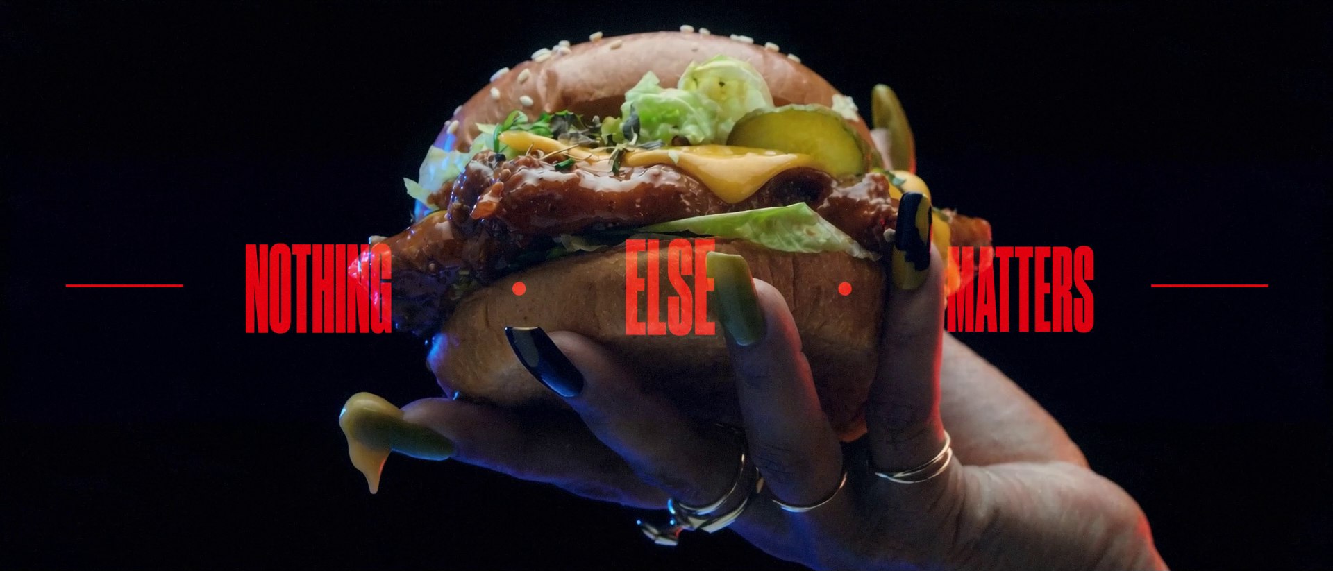 The hero product shot: a hand with long painted nails holds a dripping burger against black, 'NOTHING ELSE MATTERS' in red across it
