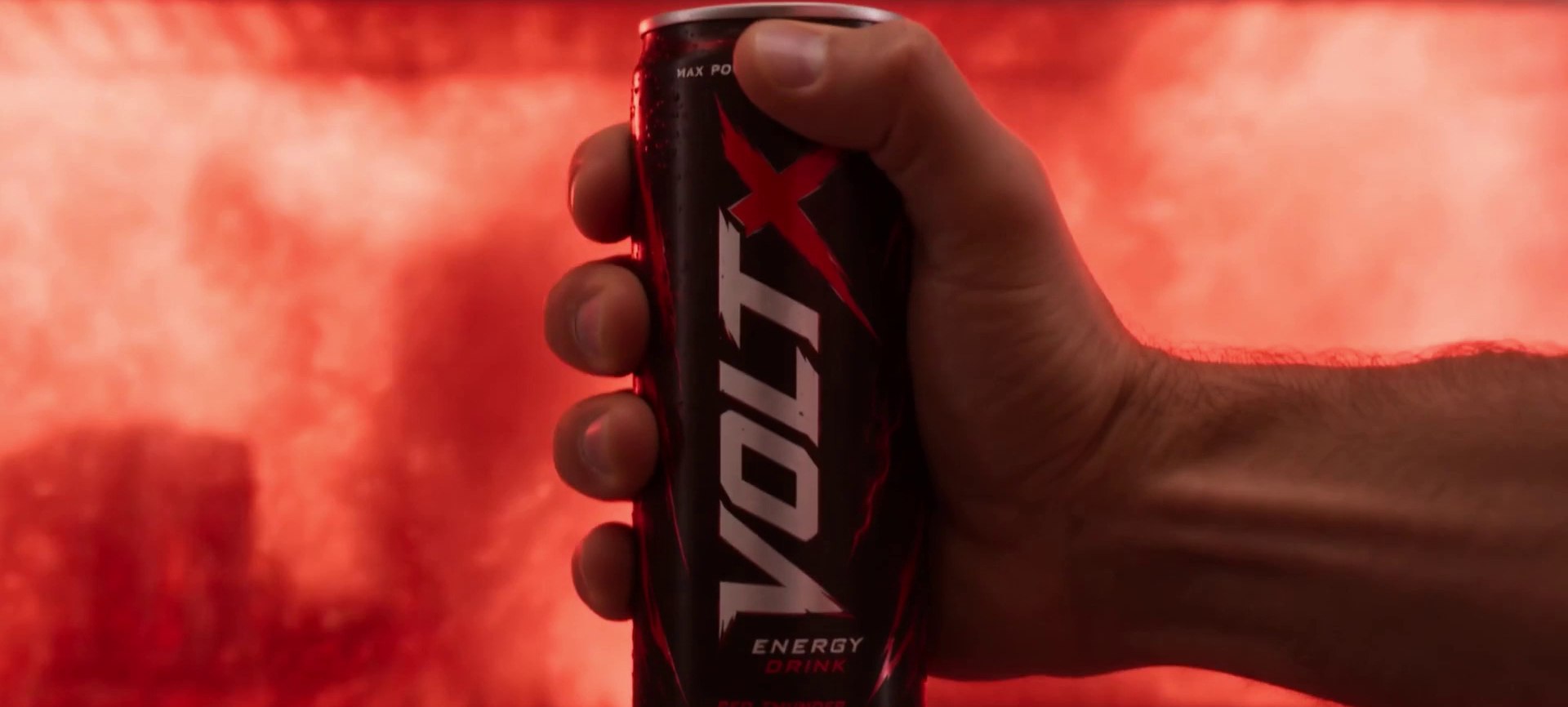 A hand raises a black and red VOLT X energy drink can against a wall of glowing red smoke